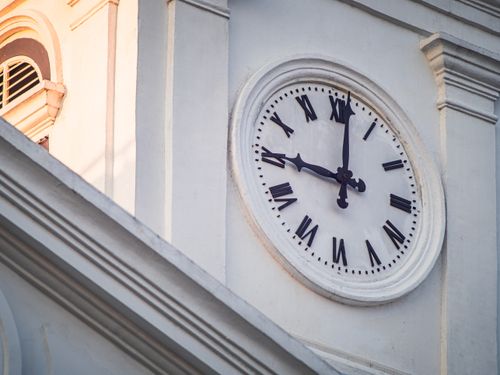 Free Close-up of a classic clock face with Roman numerals on a historic building at sunset. Stock Photo
