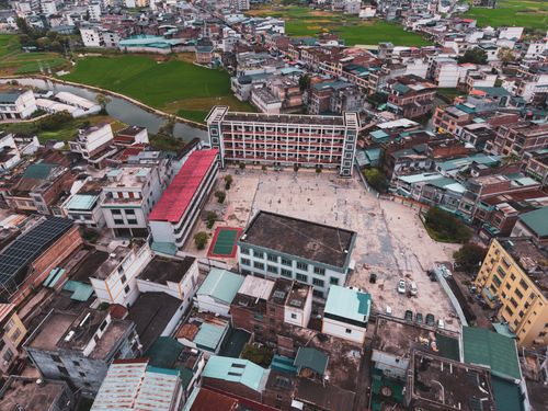 Free Aerial view of an urban neighborhood with a school at its center. Vibrant roofs and fields nearby. Stock Photo