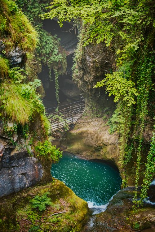 Free A tranquil cave entrance with lush greenery and a wooden bridge over a serene pool. Stock Photo