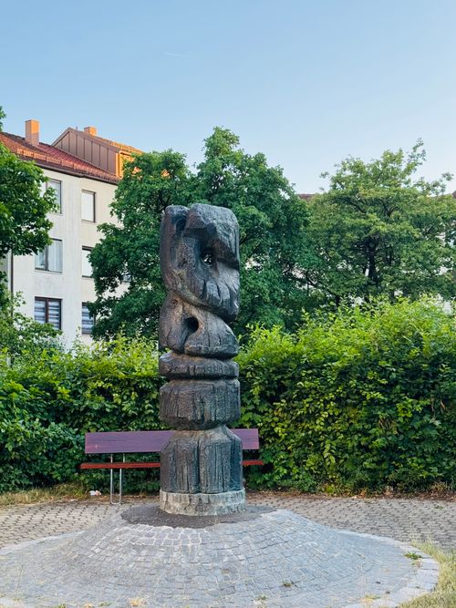 Free Abstract stone sculpture in a Munich park with green foliage and residential backdrop. Stock Photo
