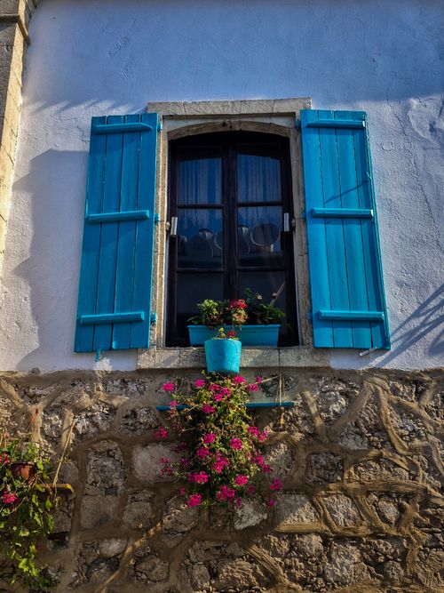 Free A picturesque Mediterranean window with vibrant blue shutters and colorful flowers in Girne. Stock Photo