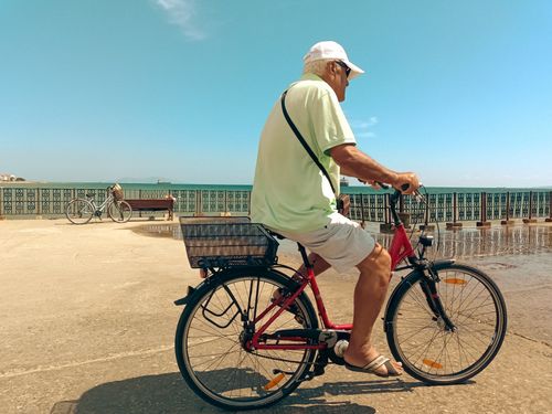Free Elderly man enjoying a leisurely bike ride along the waterfront in Şarköy, Türkiye, on a bright summer day. Stock Photo