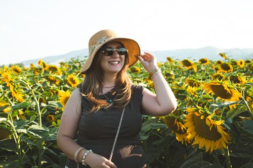Free Smiling woman in sunglasses and hat enjoying a summer day amidst blooming sunflowers. Stock Photo