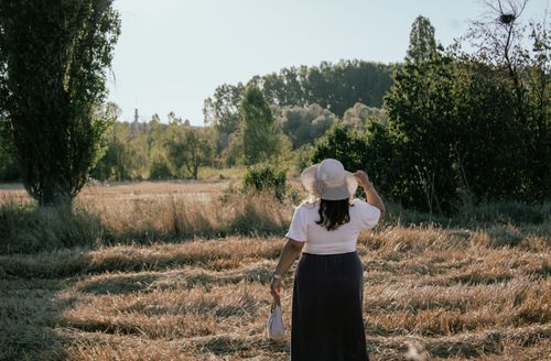 Free Woman enjoying a stroll through a serene summer field with trees. Stock Photo