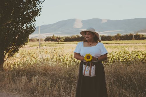 Free A woman in a summer hat holds a sunflower in a scenic wheat field with mountains in the background. Stock Photo