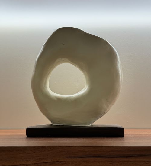 Free A unique abstract ceramic sculpture displayed on a wooden shelf with soft lighting. Stock Photo