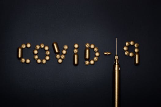 Artistic depiction of COVID-19 using pills and a syringe on a dark background, symbolizing medication.