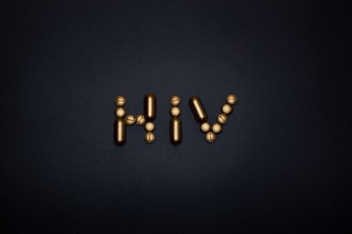Free Golden capsules form the word HIV on a dark background, symbolizing healthcare and treatment. Stock Photo