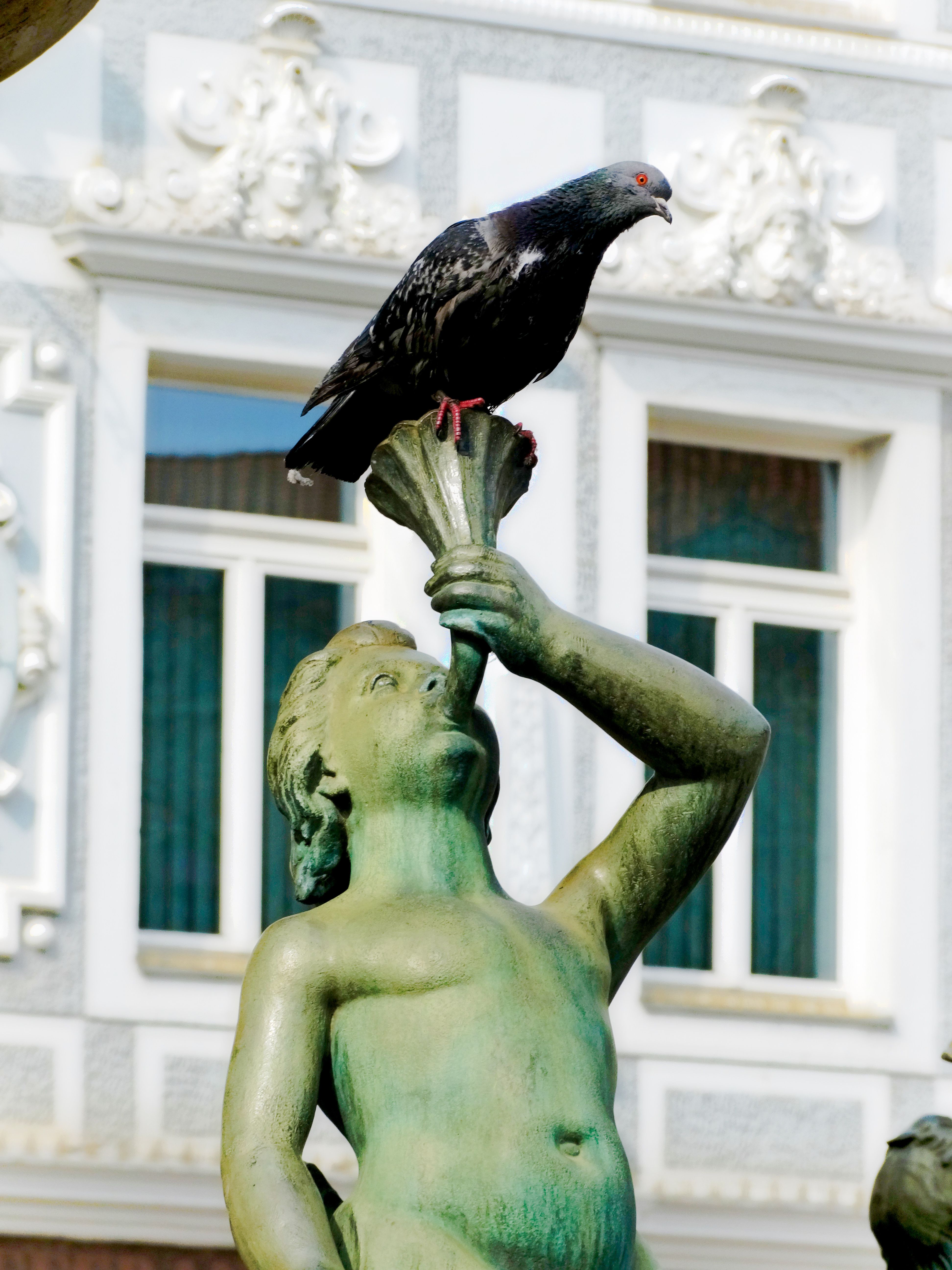 A statue in a city square with a pigeon perched on top, in bright daylight.