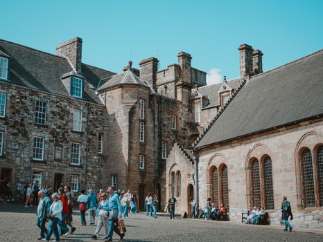 Tourists exploring the historic Stirling Castle courtyard in Scotland under a sunny sky.
