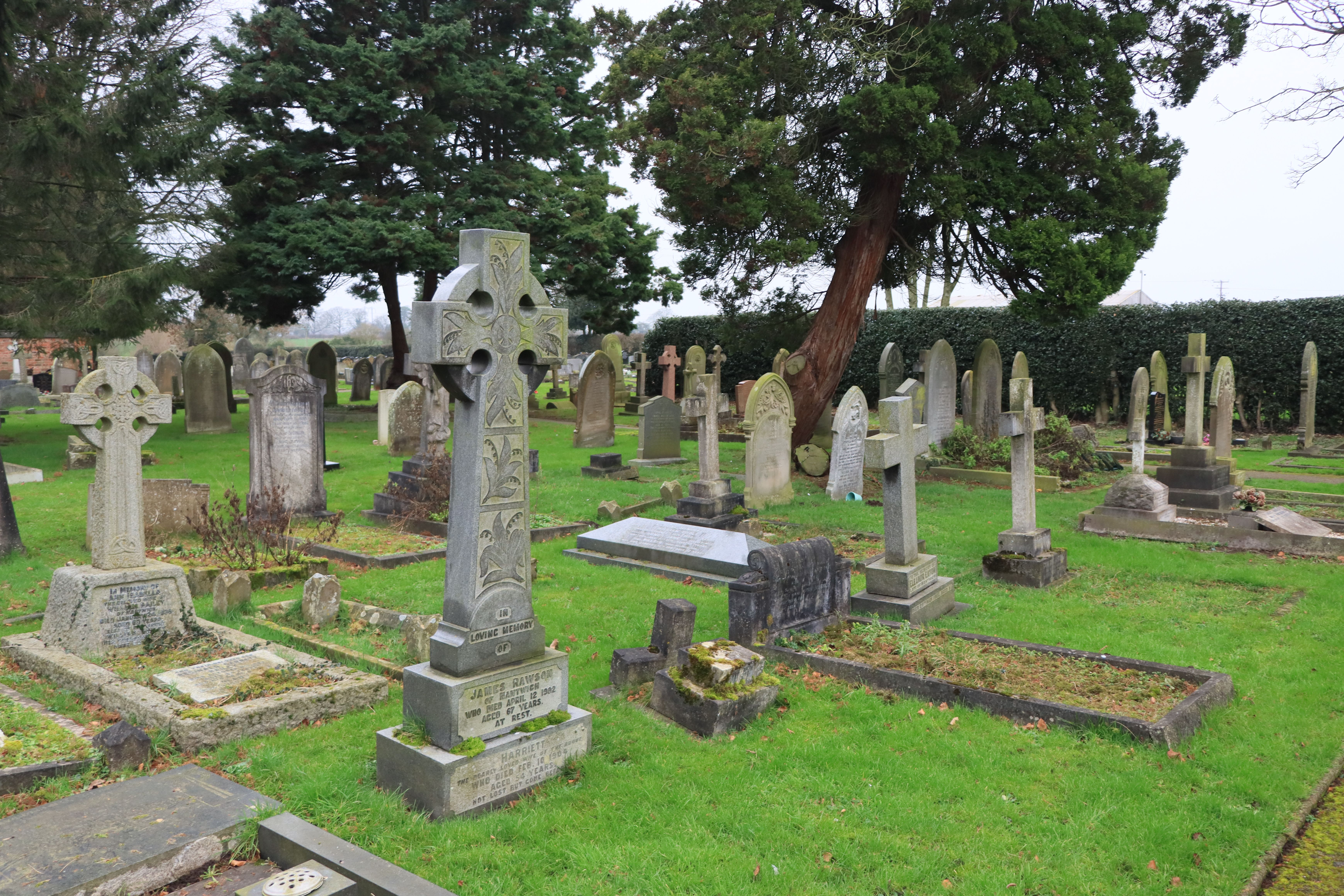A peaceful cemetery with lush greenery and ornate Celtic cross gravestones under overcast skies.