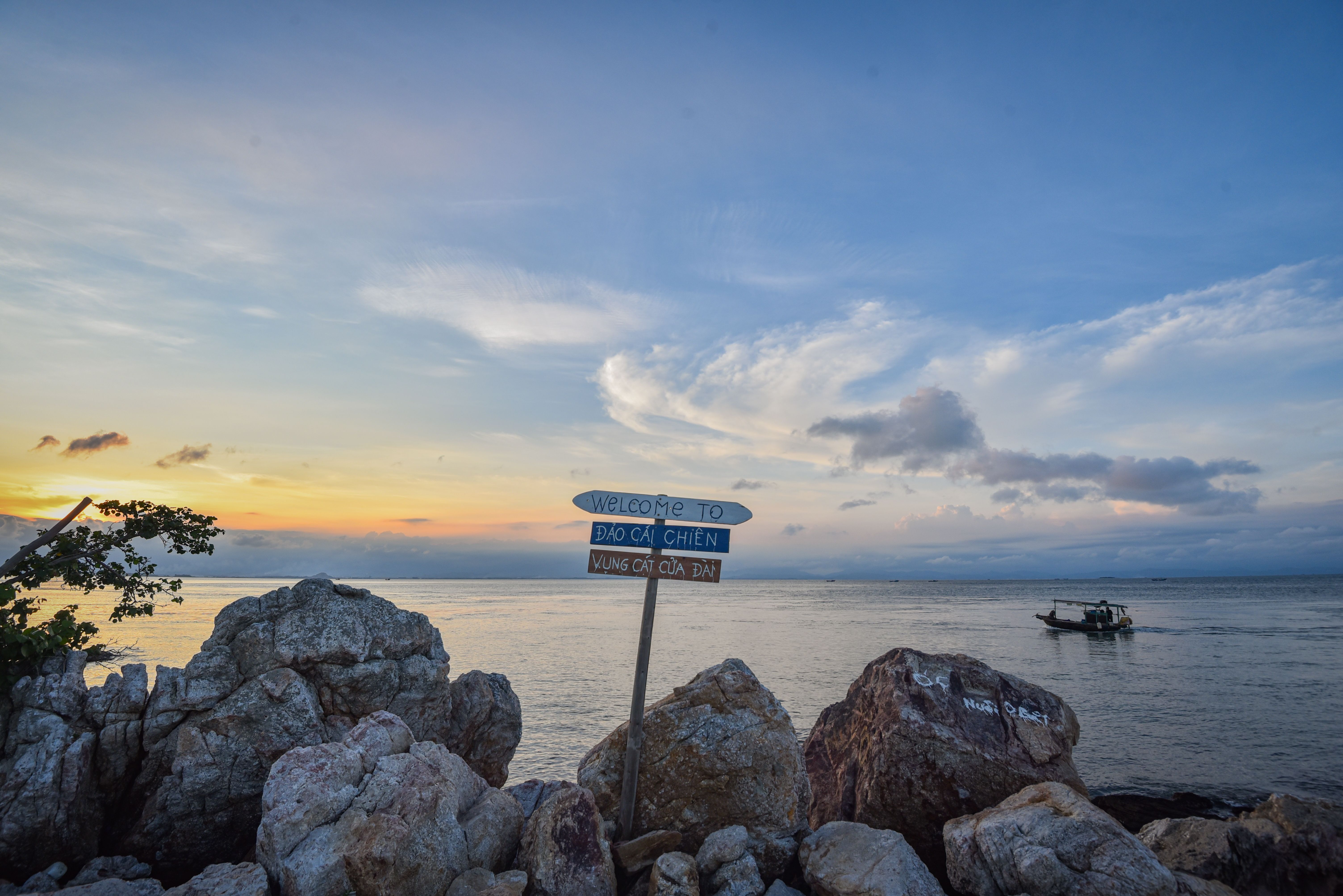 Tranquil sunset view over the rocks and sea at Cái Chiên Island in Vietnam with a boat in the distance.