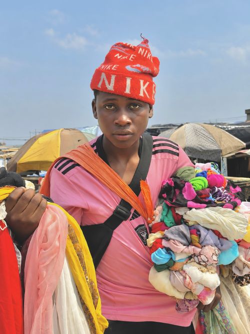 Free A young vendor displaying colorful fabrics in a bustling Lagos market. Stock Photo