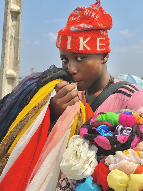 Free Young street vendor showcasing vibrant scarves on a sunny day in Lagos, Nigeria. Stock Photo