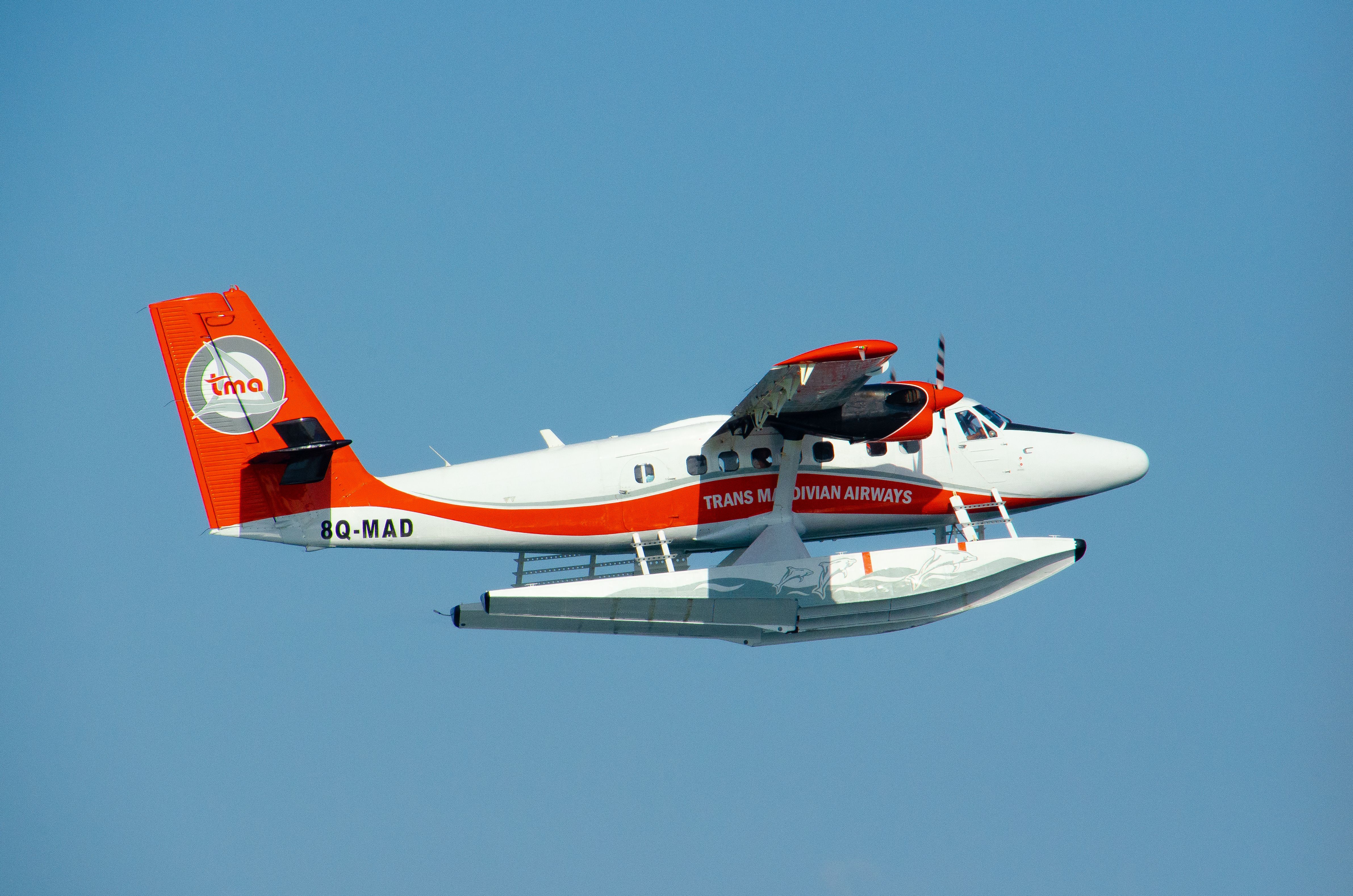 A vibrant seaplane flying over the clear skies of the Maldives, showcasing aerial transportation.