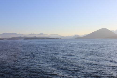 Free Peaceful view of ocean waters and mountain horizon under a glowing sunrise. Stock Photo