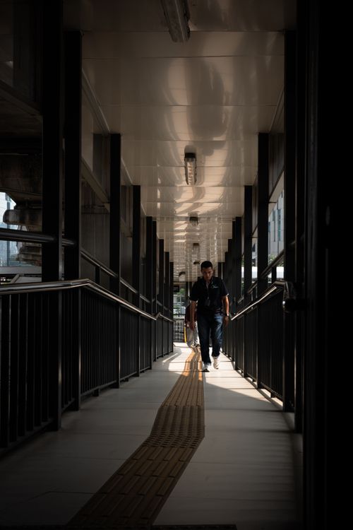 Free A solitary man walking through a covered walkway in Jakarta, Indonesia, creating a dramatic shadow play. Stock Photo