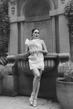 A stylish woman posing with grace by an ornate stone fountain. Fashion meets classic architecture.