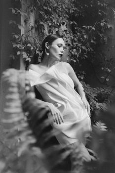 Stylish woman posing in a lush urban setting, blending fashion with nature.