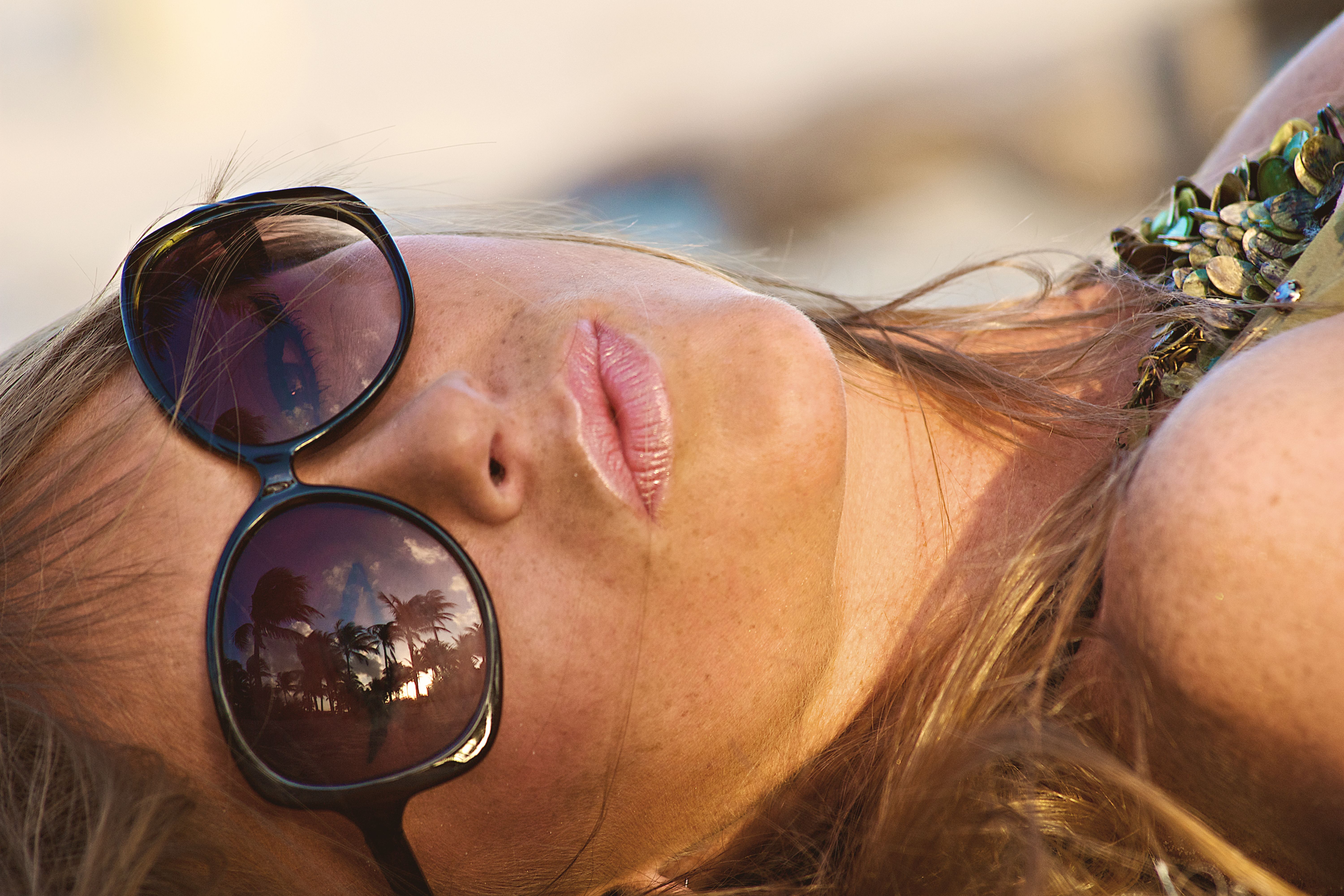 Close-up of a woman relaxing with palm tree reflections in sunglasses at Miami Beach.