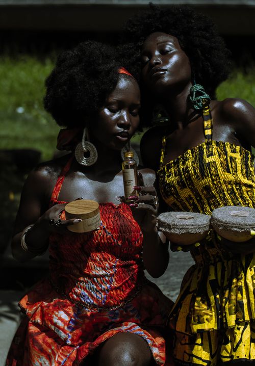 Free Two women in vibrant African dresses showcasing skincare products outdoors in Lagos. Stock Photo