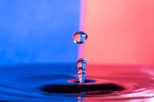 Free Close-up of a water droplet in motion, capturing reflections against a vibrant blue and red background. Stock Photo