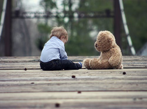 Мальчик сидит с плюшевой игрушкой бурого медведя на фото в выборочном фокусе