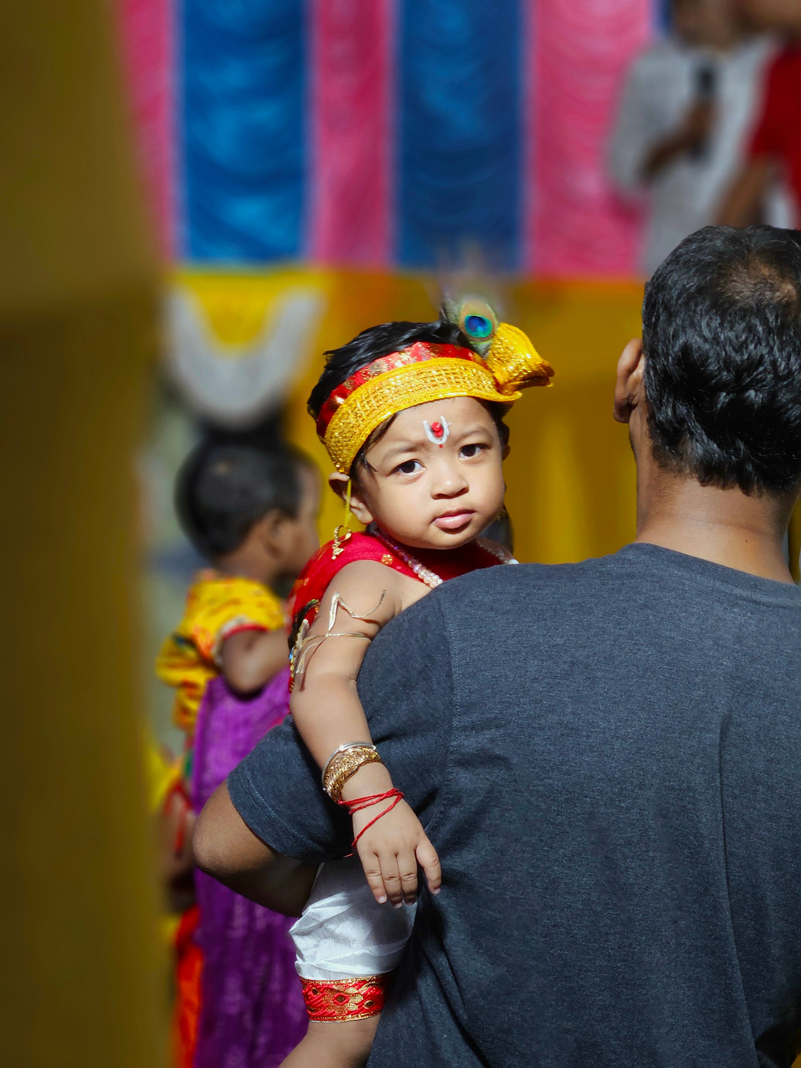 A baby in traditional attire celebrates a cultural festival indoors.