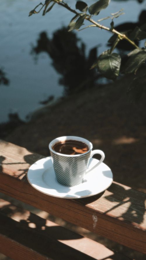 Free A peaceful Turkish coffee on a wooden railing by the water in sunlight. Stock Photo