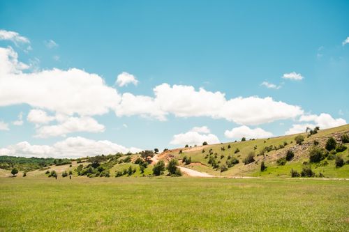 Free Expansive grassy plateau under a vibrant blue sky with rolling hills and fluffy clouds. Stock Photo