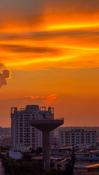Stunning sunset paints the sky in vivid orange hues over a city skyline, highlighting a prominent water tower.