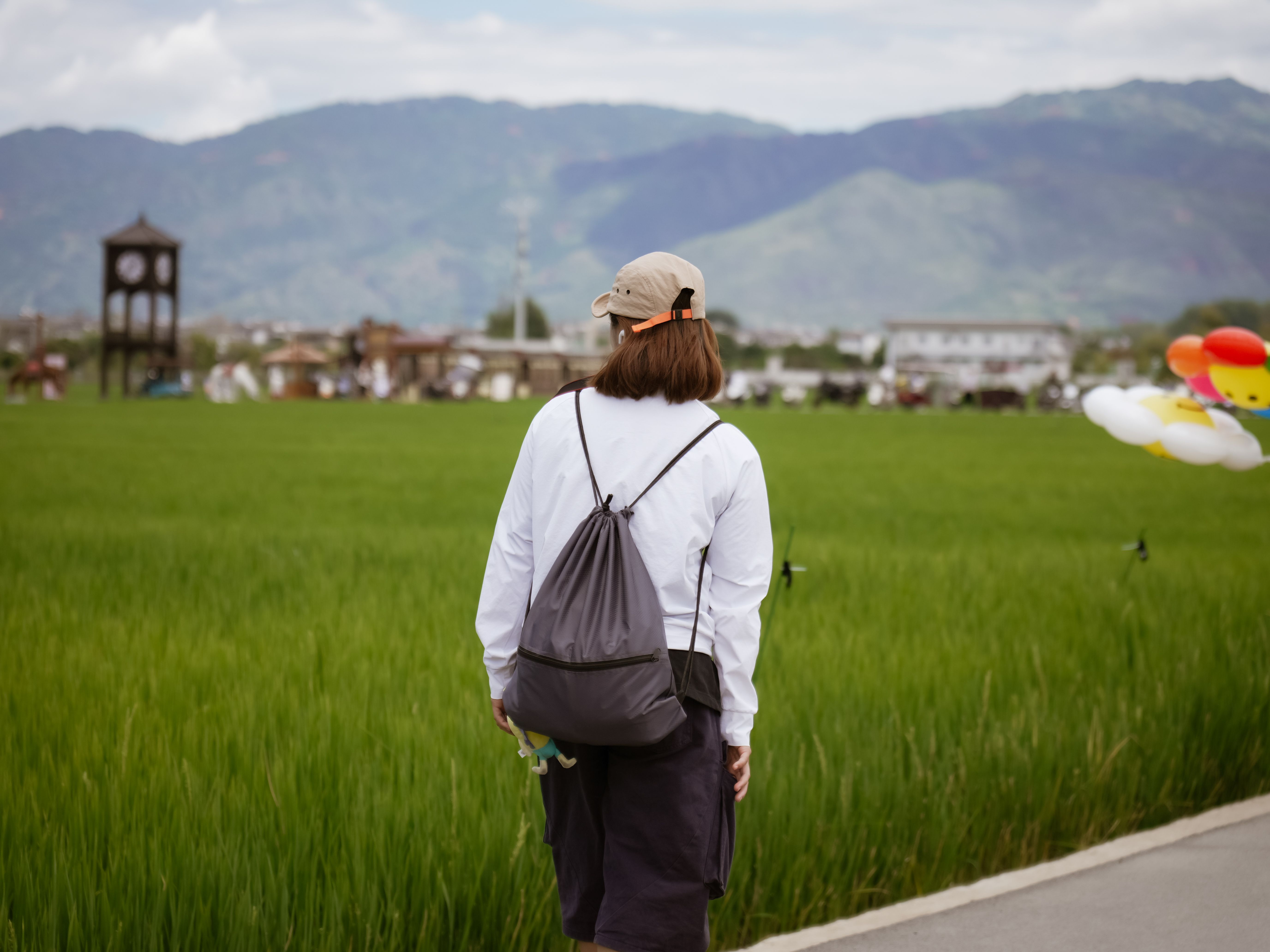 A person in casual attire explores a lush green meadow against mountain scenery.
