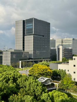 Dramatic view of a modern skyscraper surrounded by trees in Shanghai, under a cloudy sky.