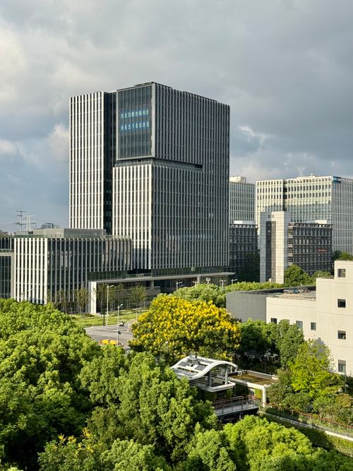 Free Dramatic view of a modern skyscraper surrounded by trees in Shanghai, under a cloudy sky. Stock Photo