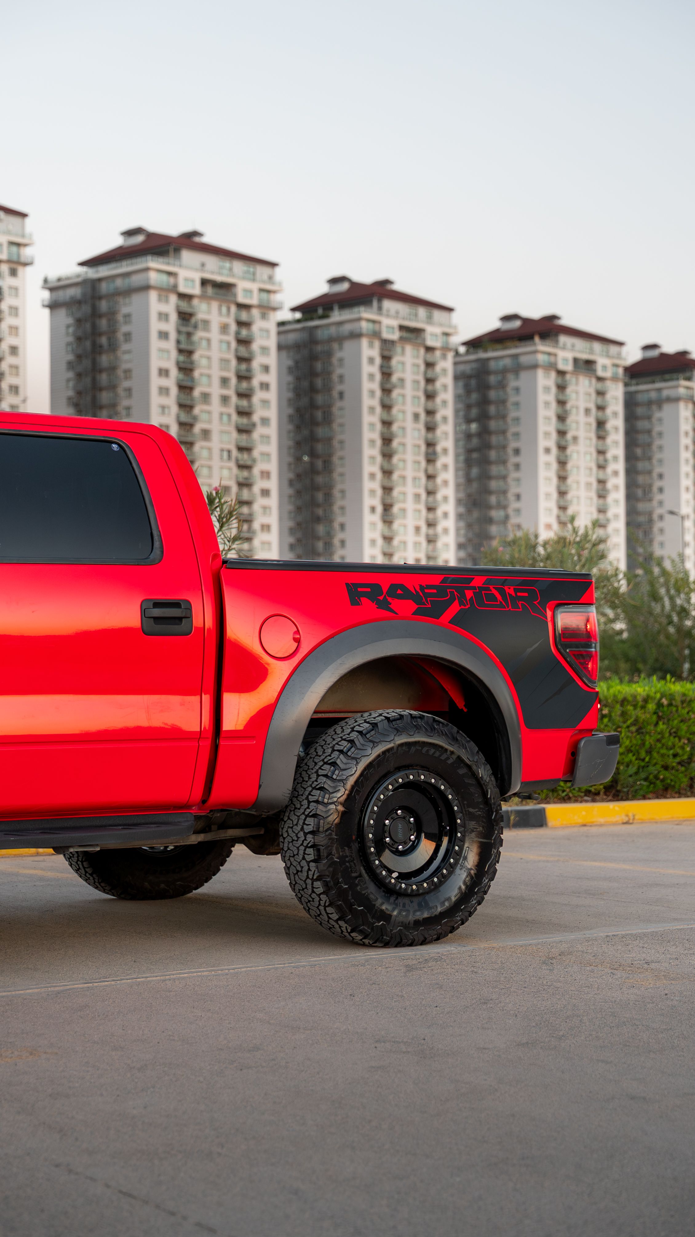 Fotomural Camioneta roja estacionada con edificios altos al fondo en un día despejado.