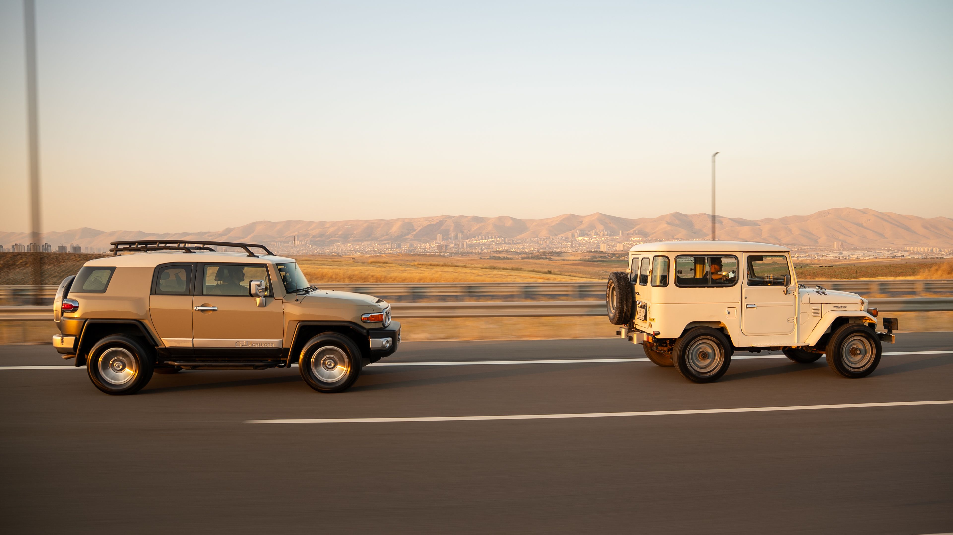 Two SUVs driving on a highway near mountains in daylight