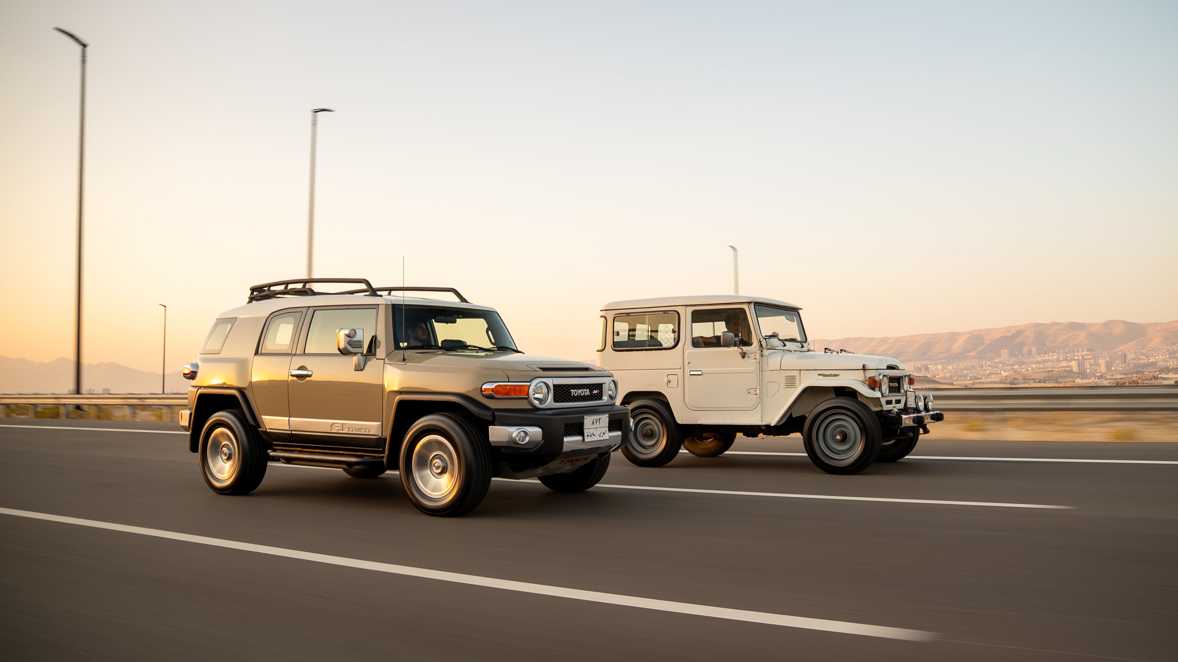 Side view of classic and modern SUVs driving on a freeway at sunset