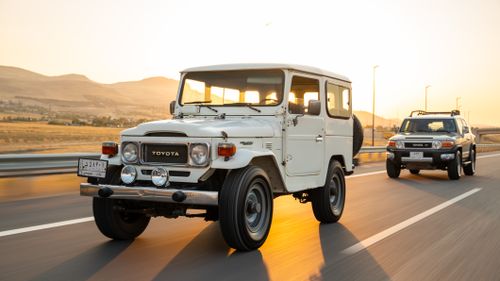 Free A classic Toyota Land Cruiser driving on a highway with scenic mountains in the sunset background. Stock Photo