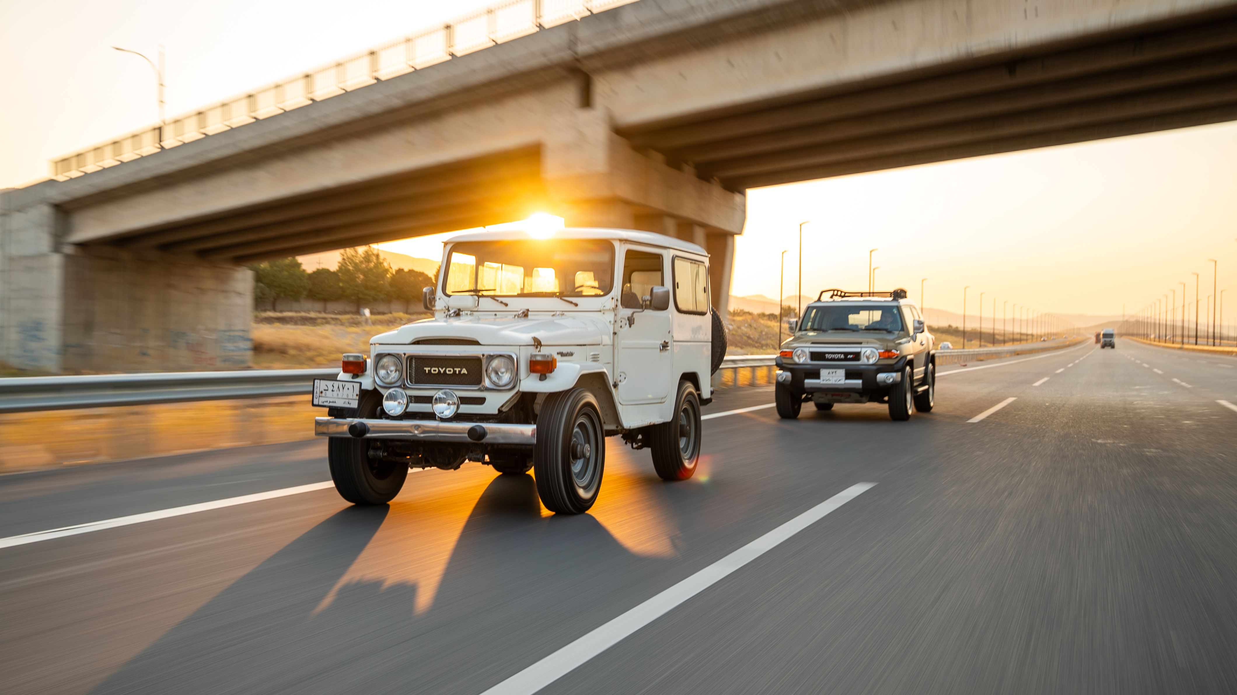 Vintage Toyota Land Cruiser driving on a highway at sunset under a bridge, showcasing adventure and freedom.