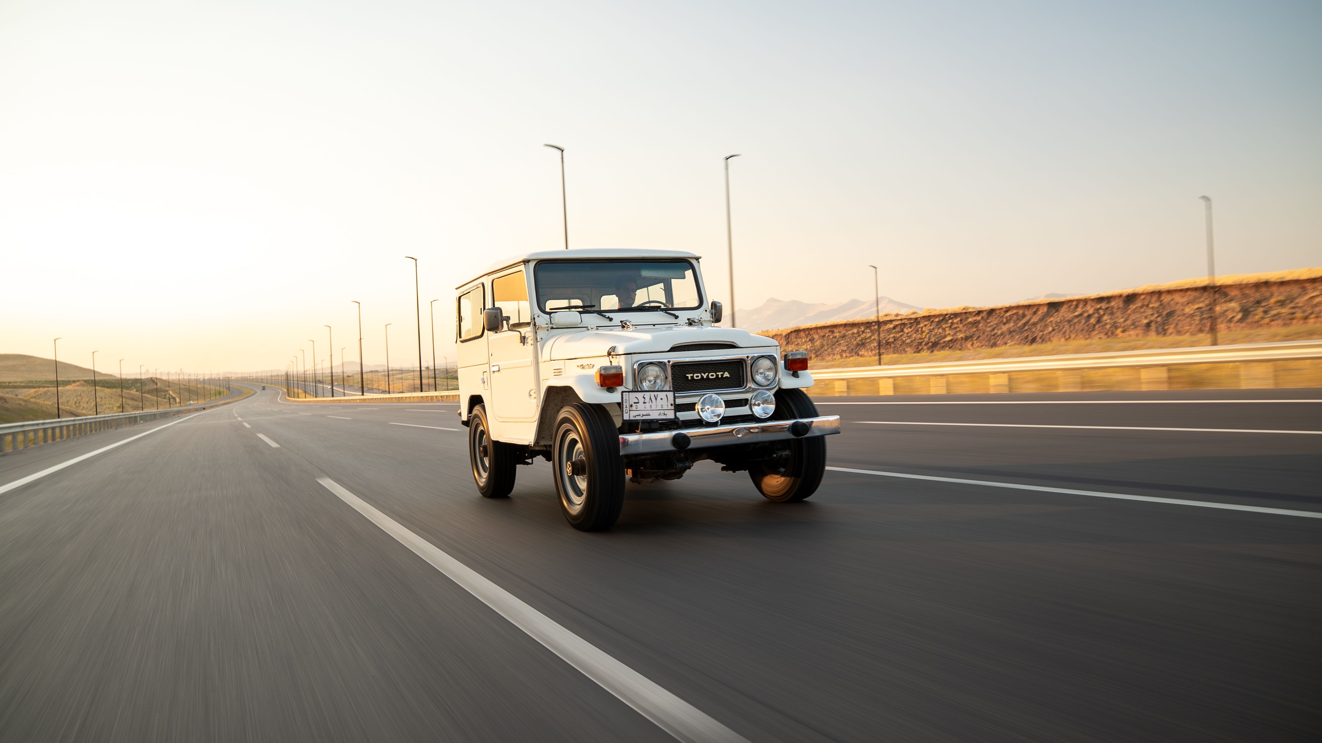 White SUV traveling on an empty highway at sunrise