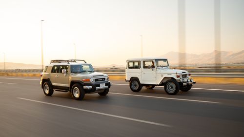 Free Two classic Toyota SUVs driving side by side on a highway at sunset, with mountains in the background. Stock Photo