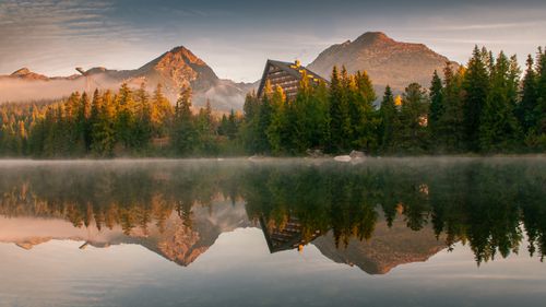 Free Beautiful reflection of High Tatras mountains and hotel in Štrbské Pleso lake at sunrise. Stock Photo