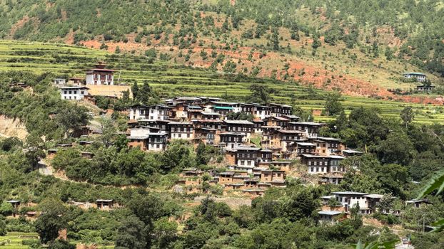 A picturesque Bhutanese village nestled on a hillside surrounded by lush greenery.