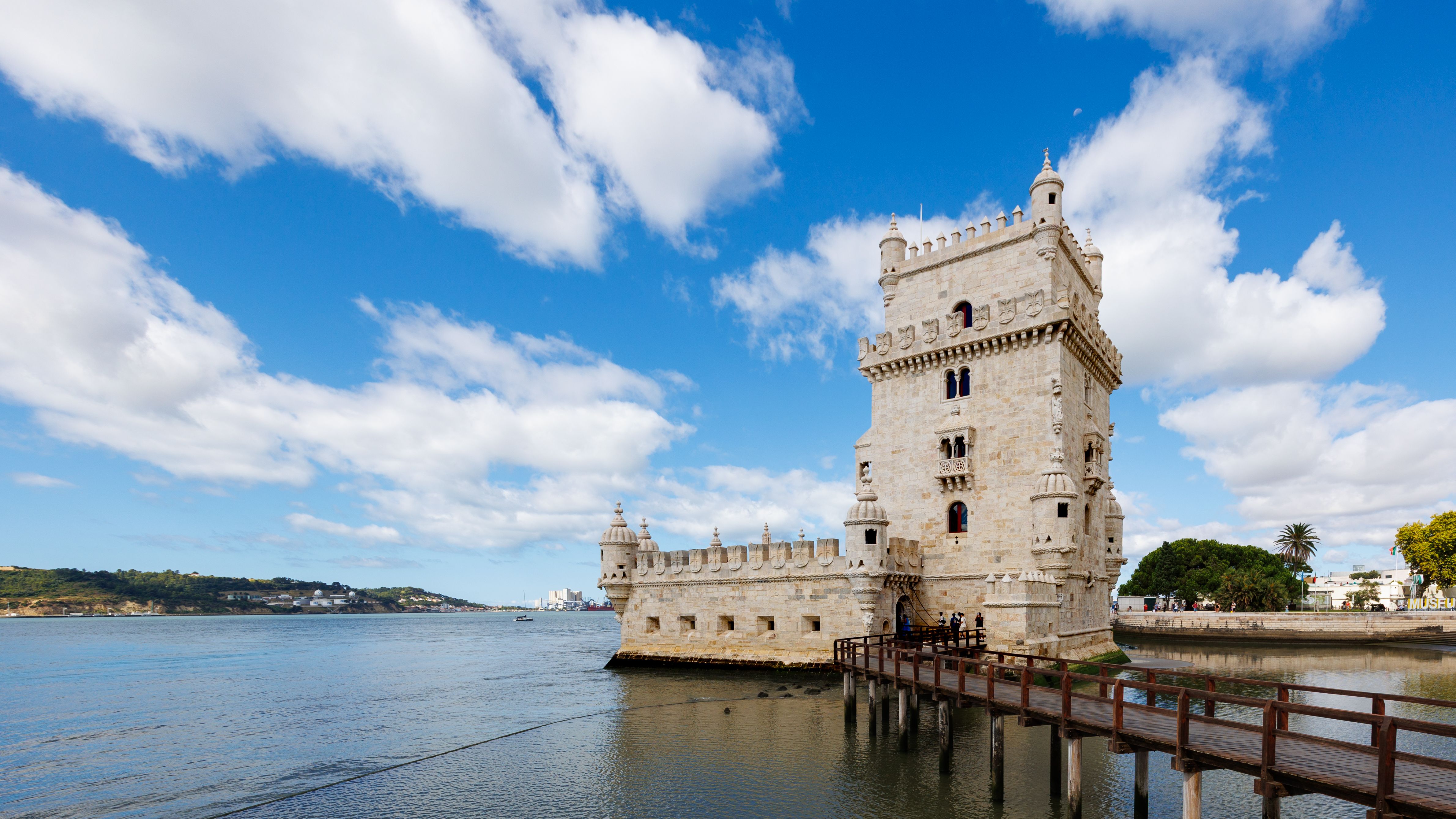 A scenic view of the historic Torre de Belém by the Tagus River in Lisbon, Portugal, under a clear blue sky.