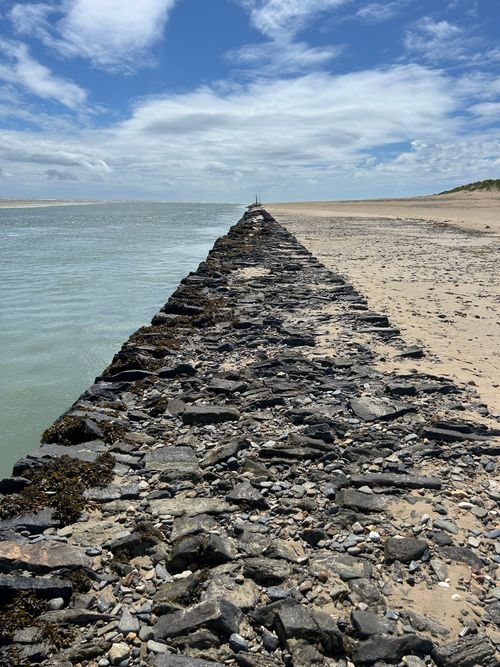 Free A rocky jetty extends along a serene beach in France, with blue skies and gentle waves. Stock Photo