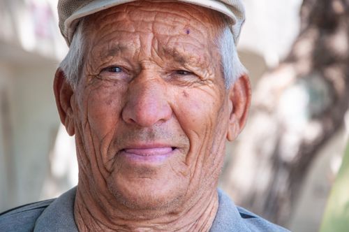 Free Close-up portrait of a smiling elderly man wearing a cap outdoors. Stock Photo