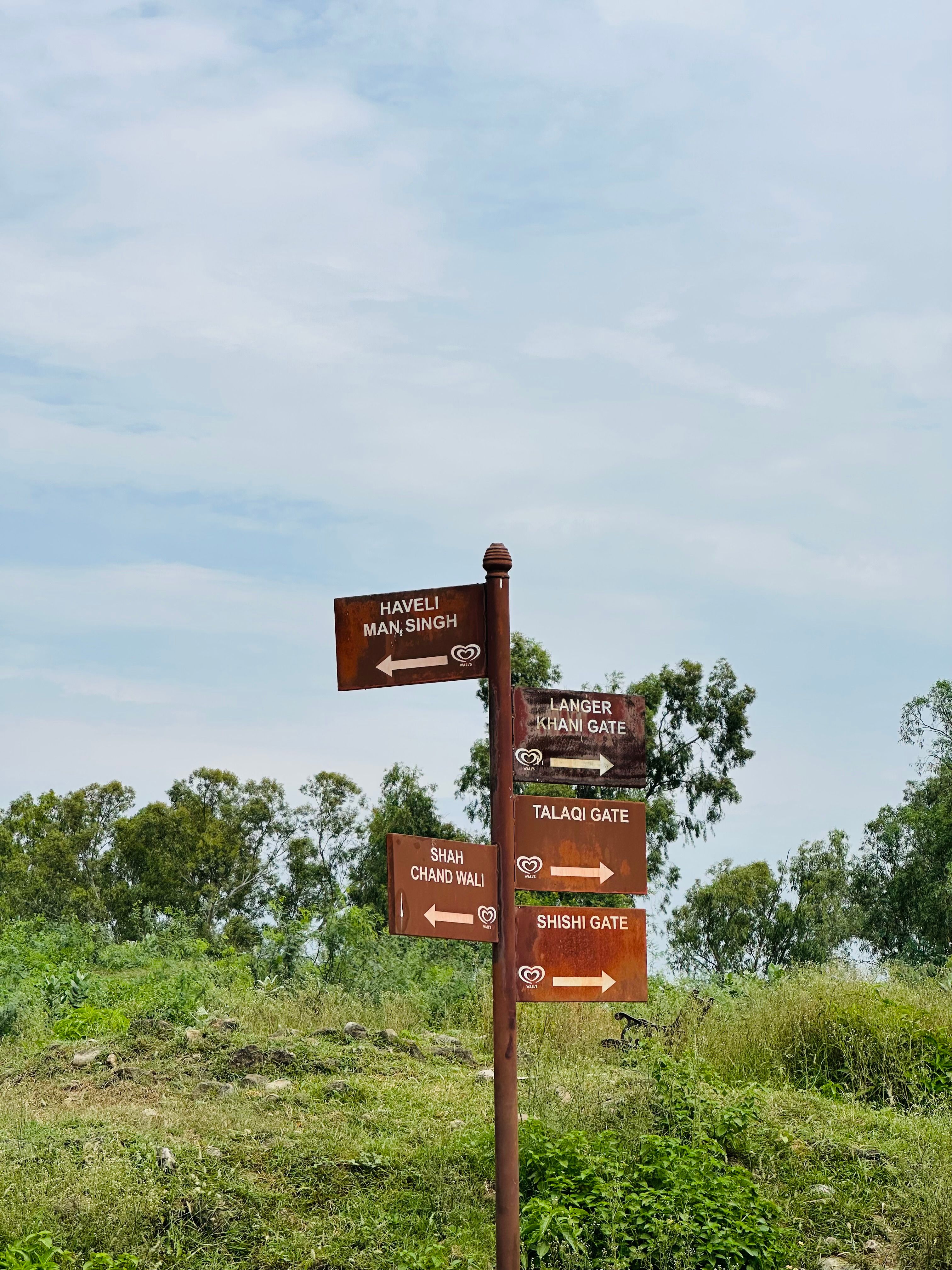 Signpost at Rohtas Fort, Pakistan, against a lush green background and cloudy sky.