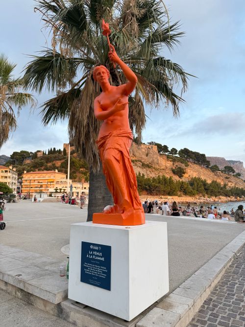 Free Vibrant orange statue on Cassis coastline with palm trees and cliffs in Provence, France. Stock Photo