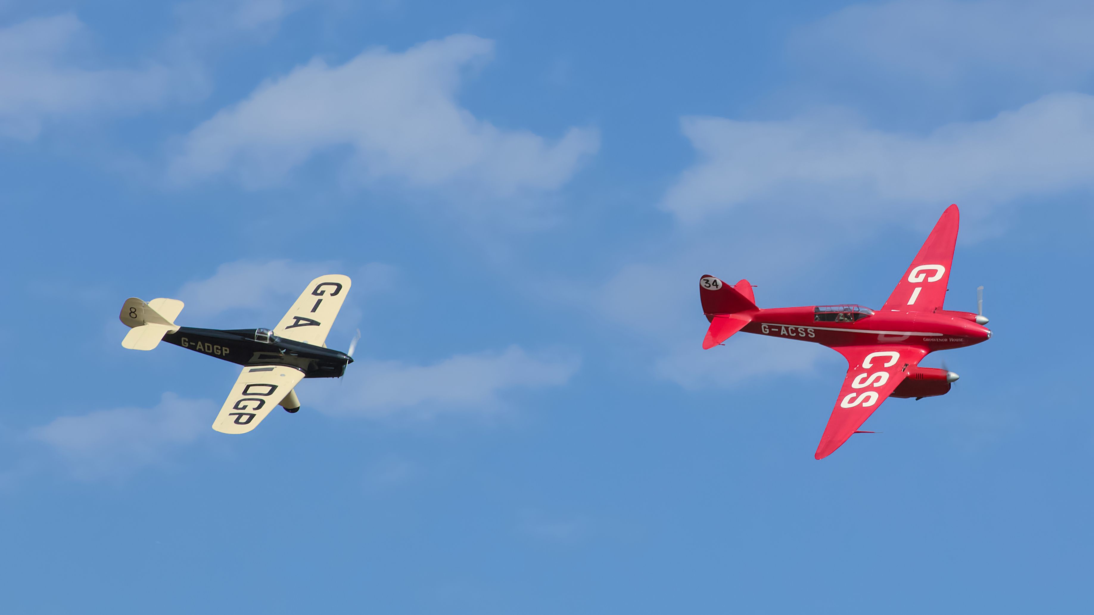 Two vintage aircraft performing in clear blue skies, showcasing classic aviation style.