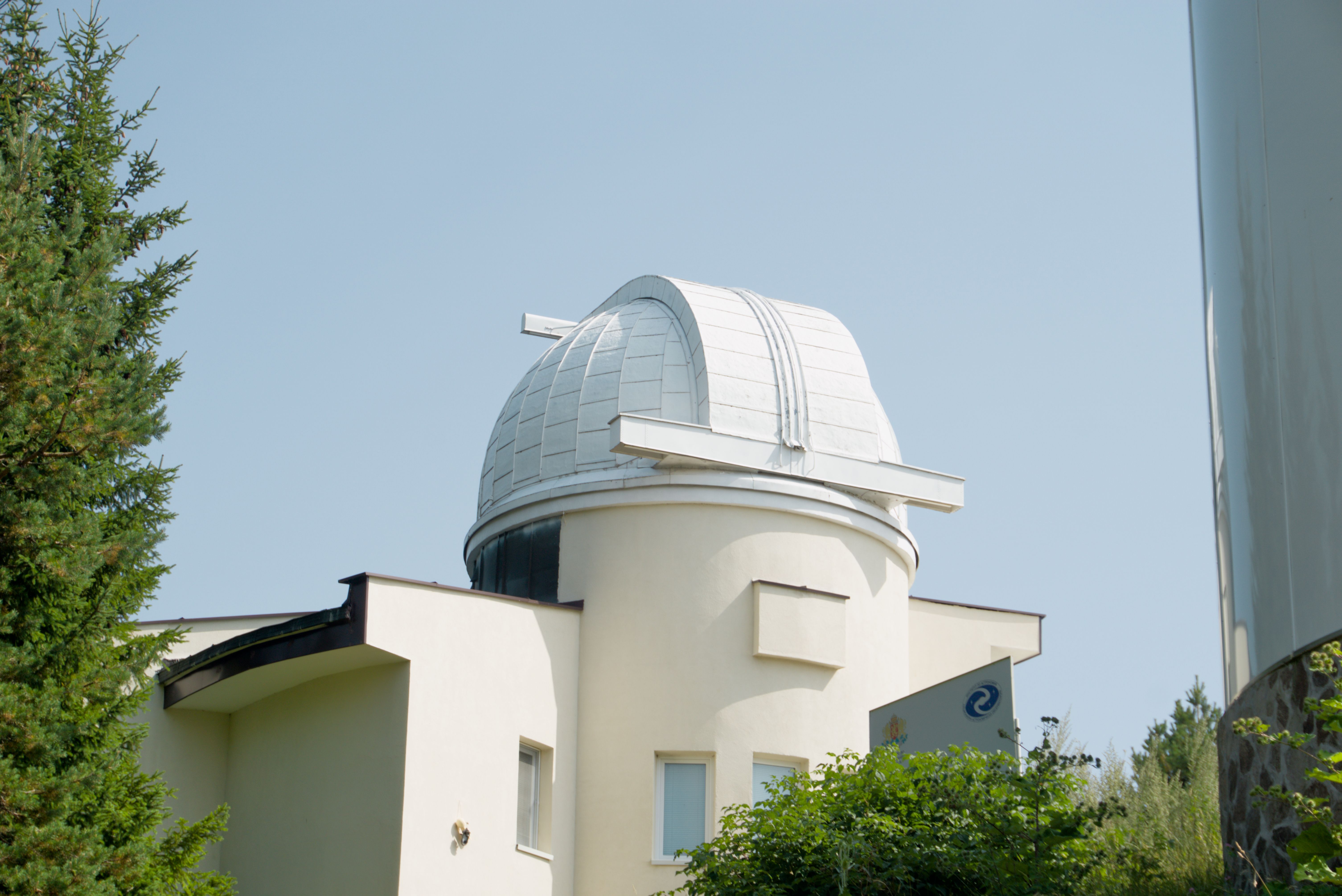 White observatory dome surrounded by lush green trees in Pamporovo, Bulgaria under a clear sky.